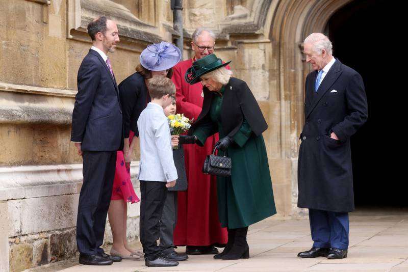 WINDSOR, ENGLAND - MARCH 31: King Charles III watches as Queen Camilla receives some flowers from a boy as they leave after attending the Easter Mattins Service at Windsor Castle on March 31, 2024 in Windsor, England. (Photo by Hollie Adams - WPA Pool/Getty Images)