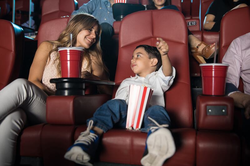 Kid sitting in the cinema theater with his parents and getting excited about the movie